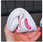 White kids sneaker with pink 'Fashion' tag, soft sole, held in hand for size view